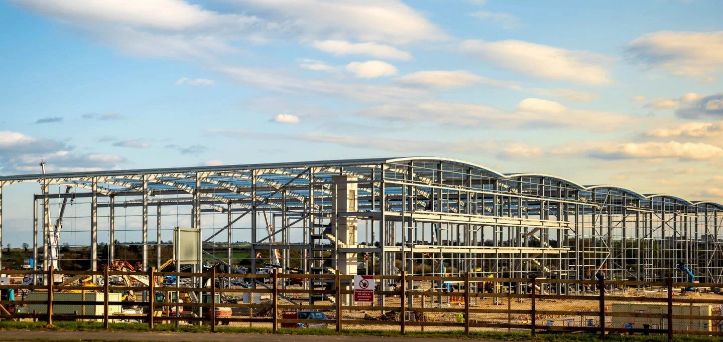 A steel-framed building under construction behind a site fence
